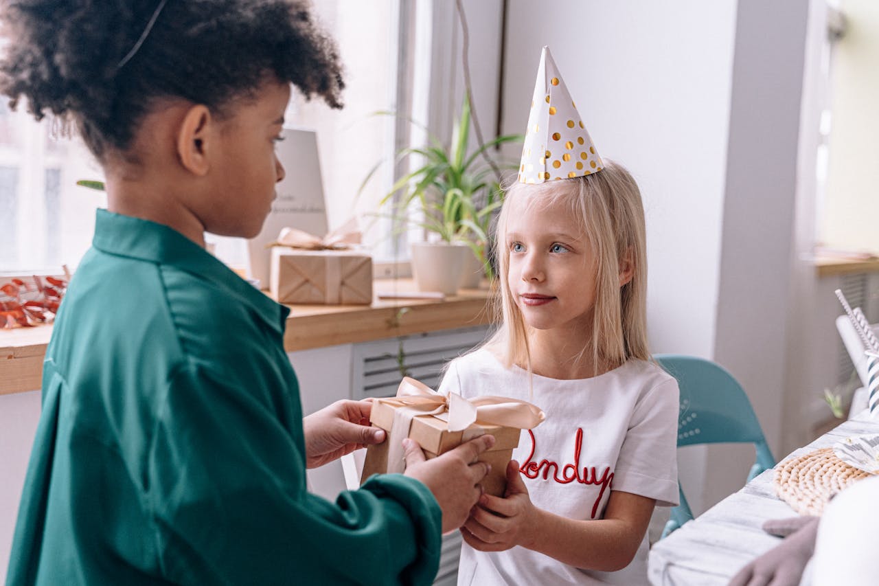 A joyful moment of children exchanging a gift during a birthday celebration indoors, highlighting friendship and fun.